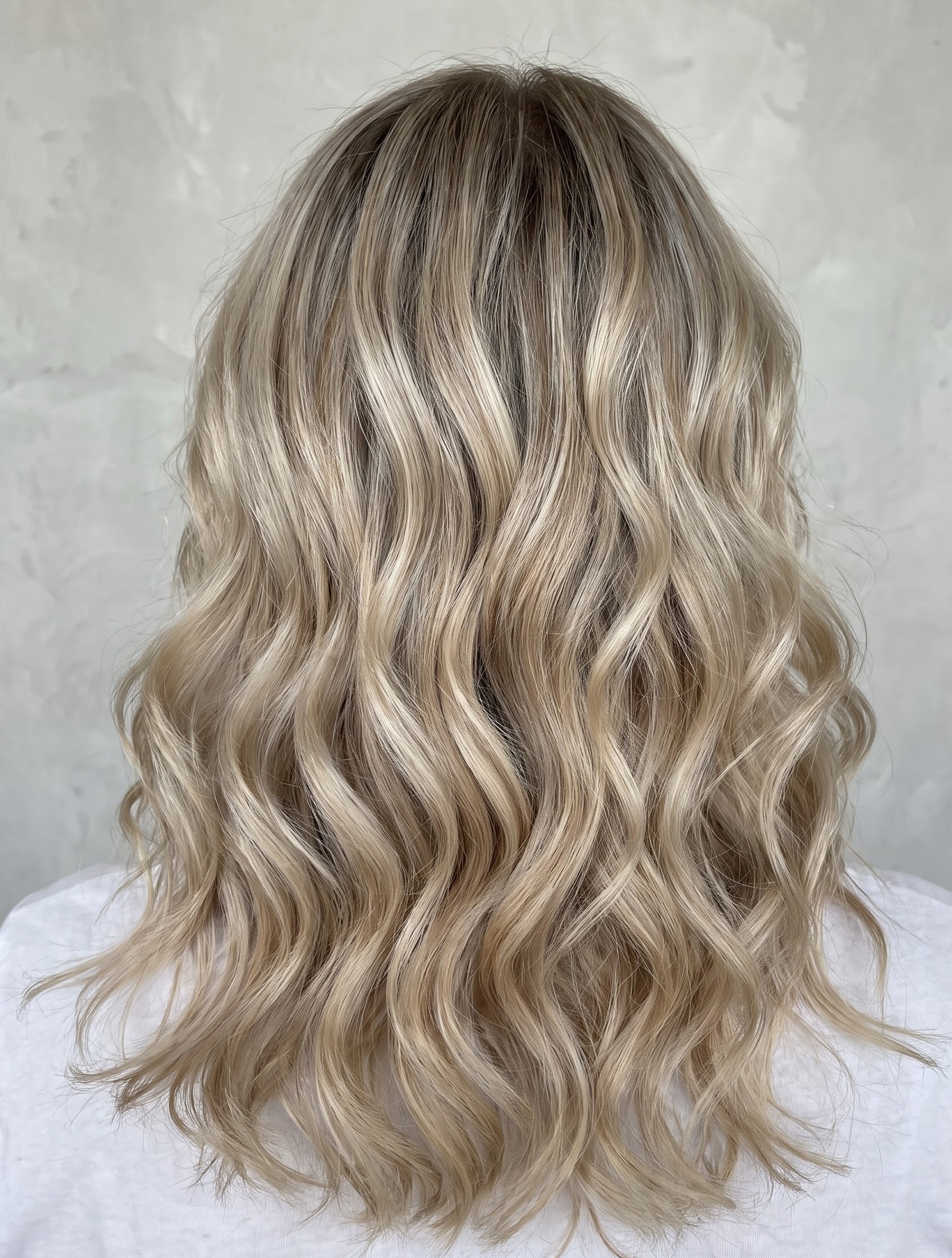 Ash blonde balayage hair styled in loose waves against a plain neutral backdrop