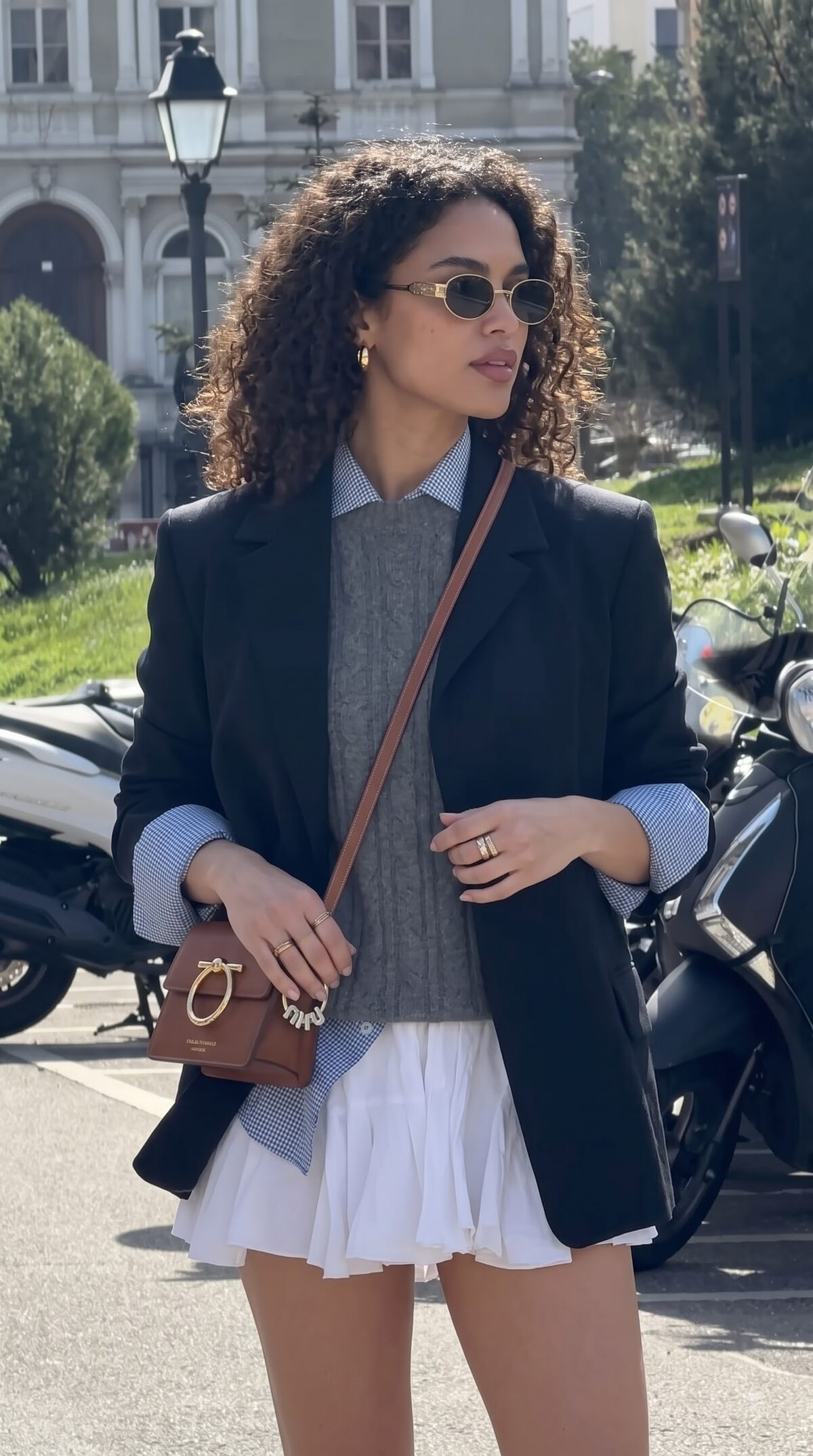 Tailored black jacket layered over a grey cardigan and white pleated skirt