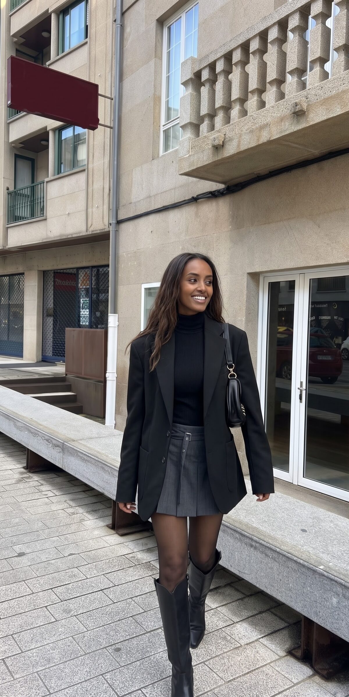 Oversized black jacket styled with a grey pleated mini skirt and knee-high boots
