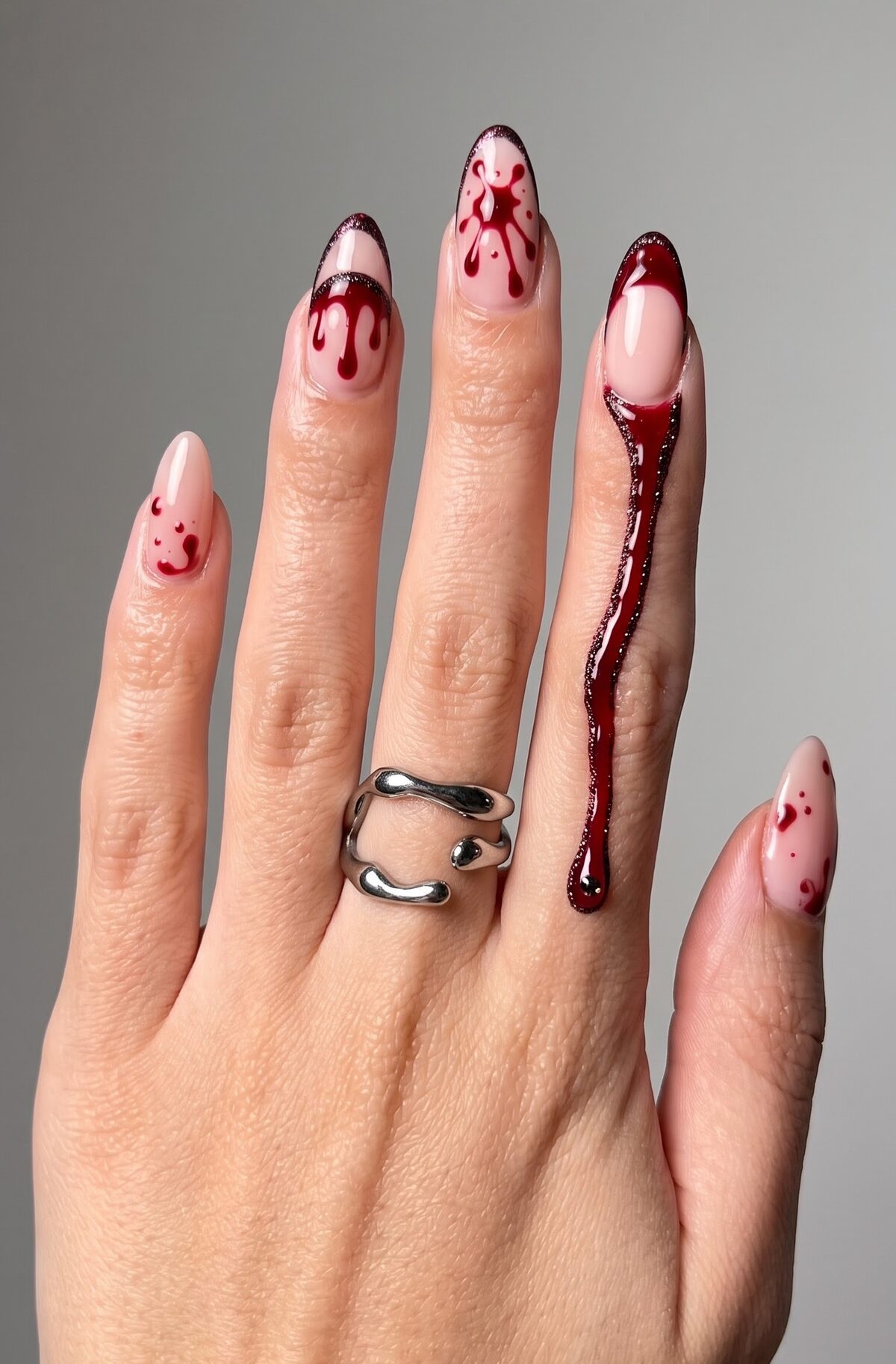 Nude nails with painted red blood splatter and drip art plus a glitter drip accent nail