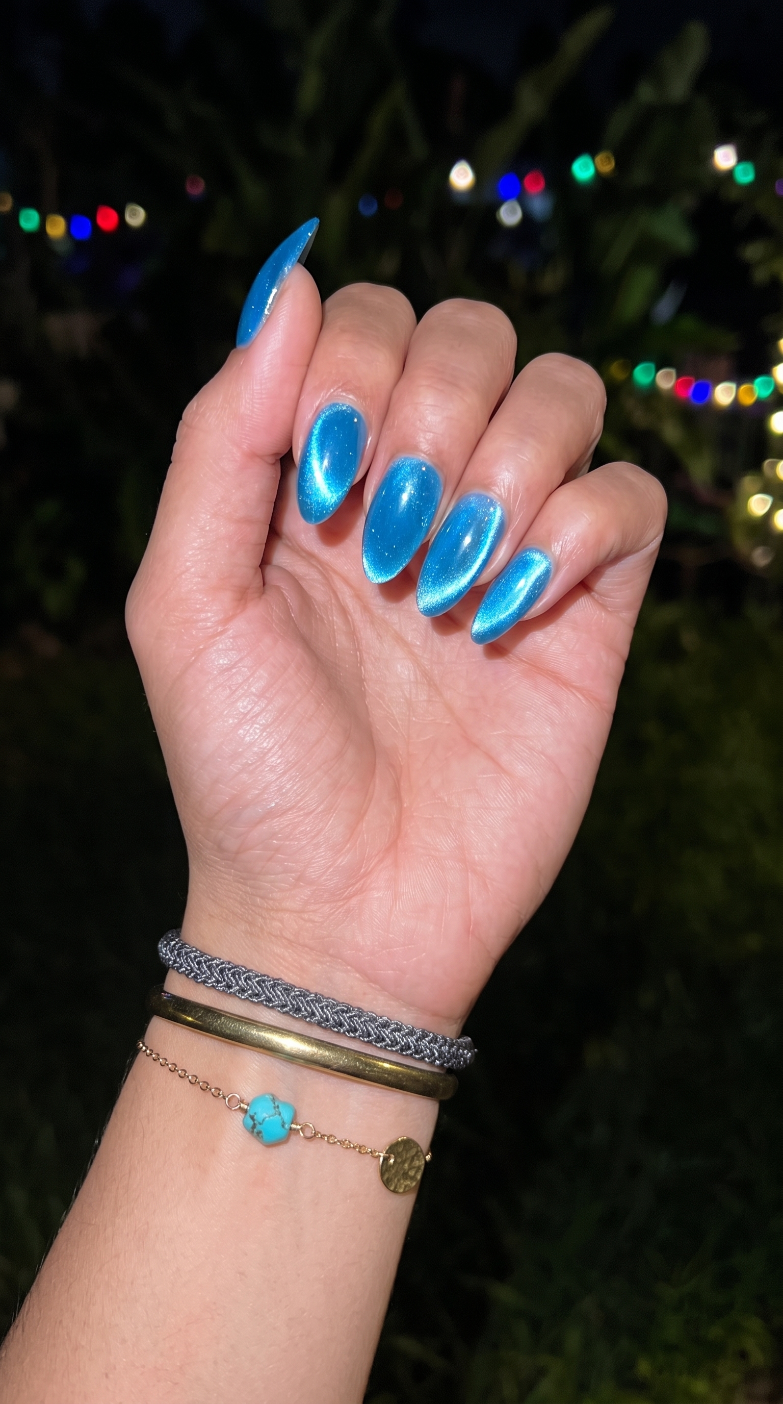 Blue cat eye magnetic chrome nails at night with festival lights and stacked bracelets