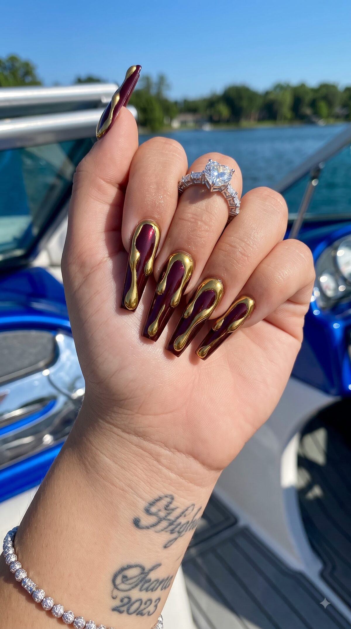 Long burgundy chrome coffin nails with liquid gold drip art along the edges