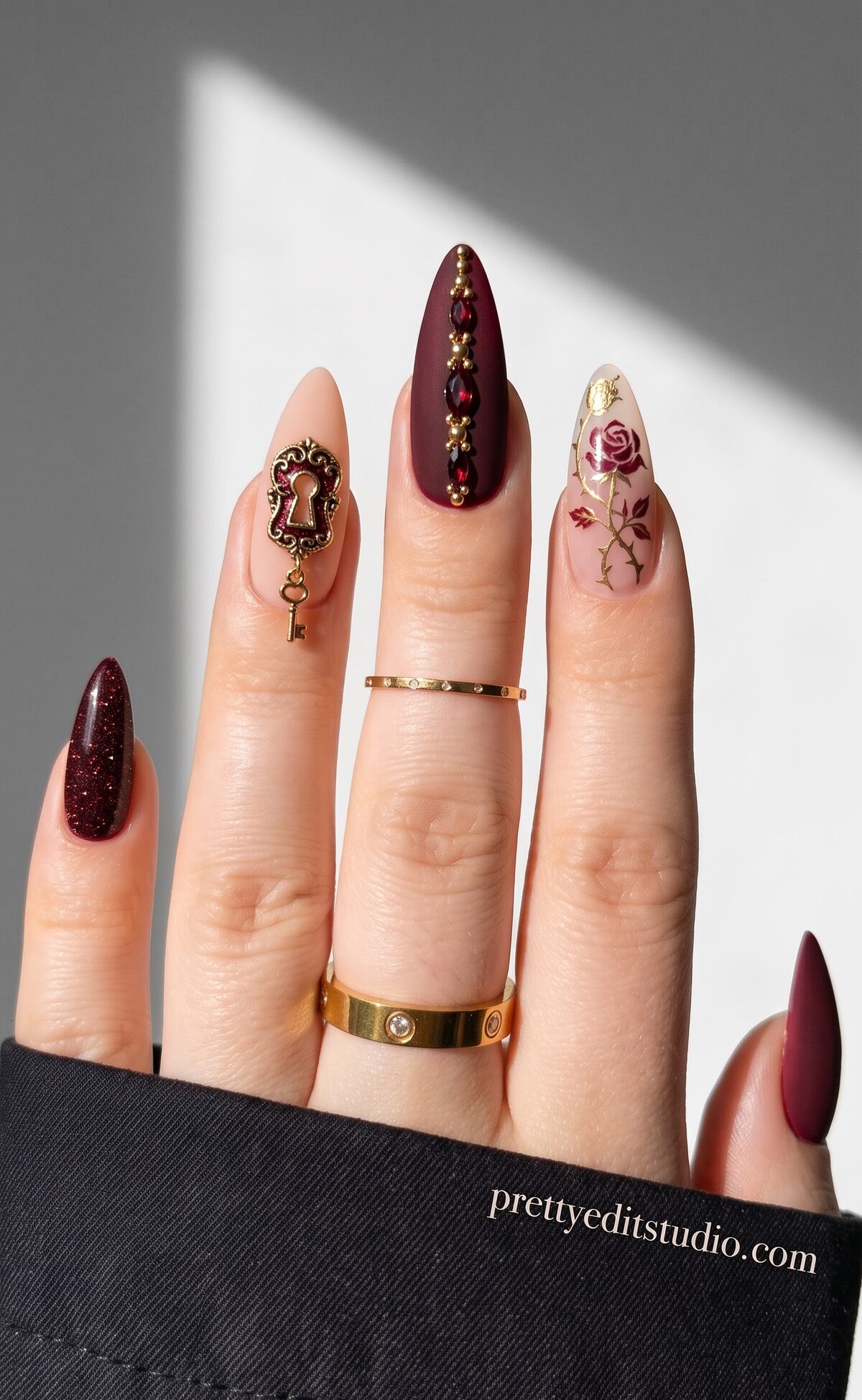 Burgundy matte nails with gold bead detailing, a keyhole charm and a gold rose vine