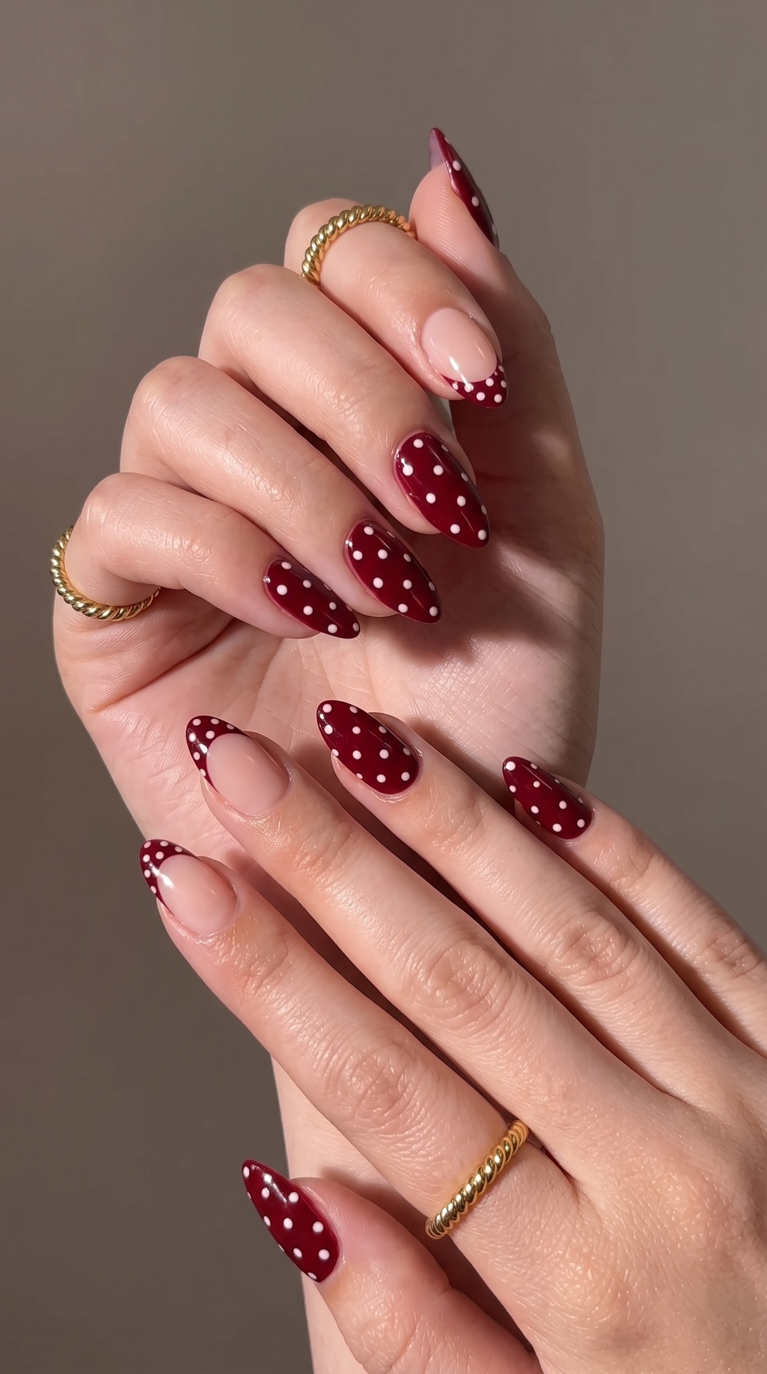 Burgundy polka dot almond nails with nude French tip and gold twisted rings