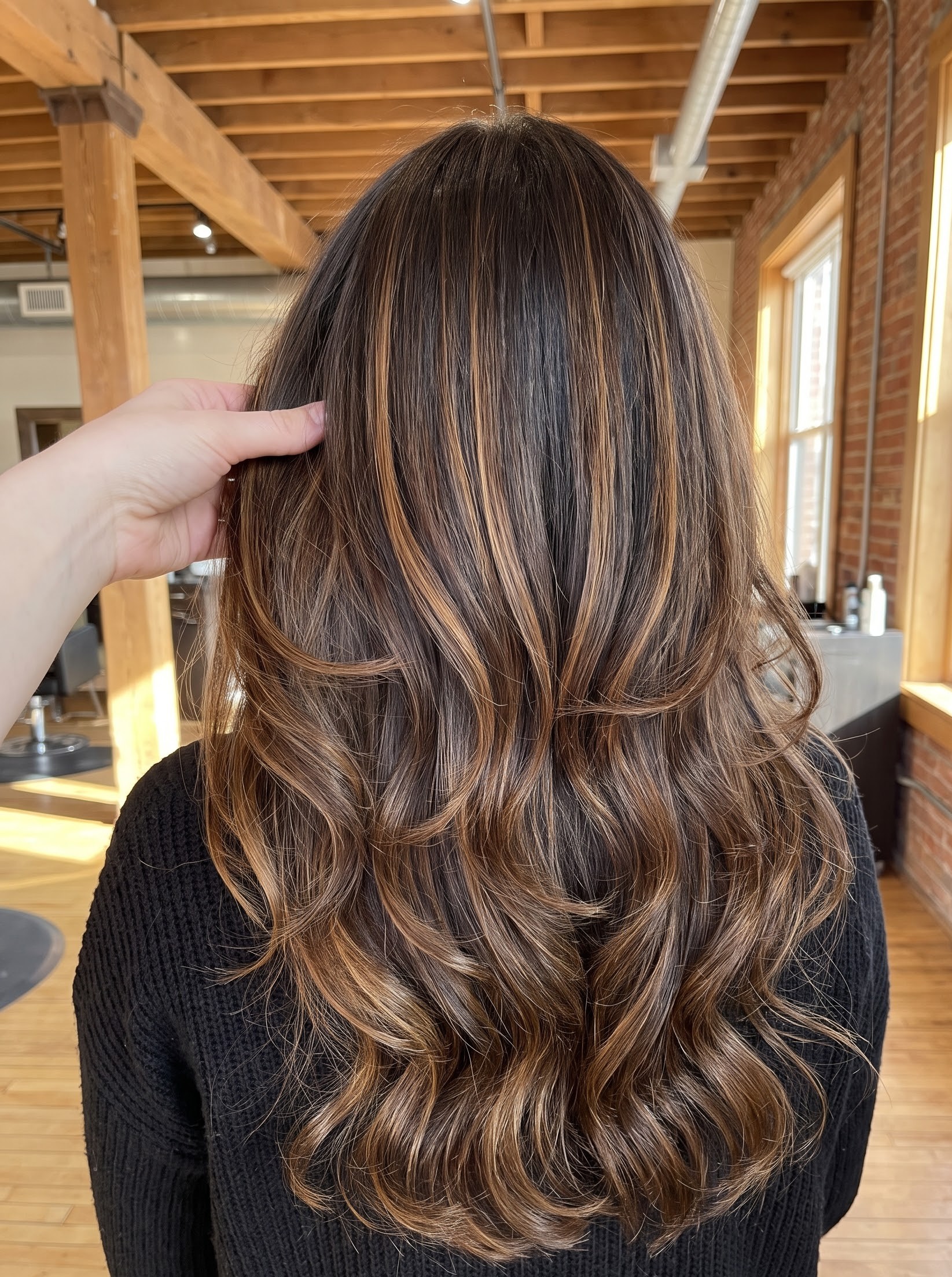 Brunette hair with caramel balayage highlights and loose curls, styled in an industrial loft salon