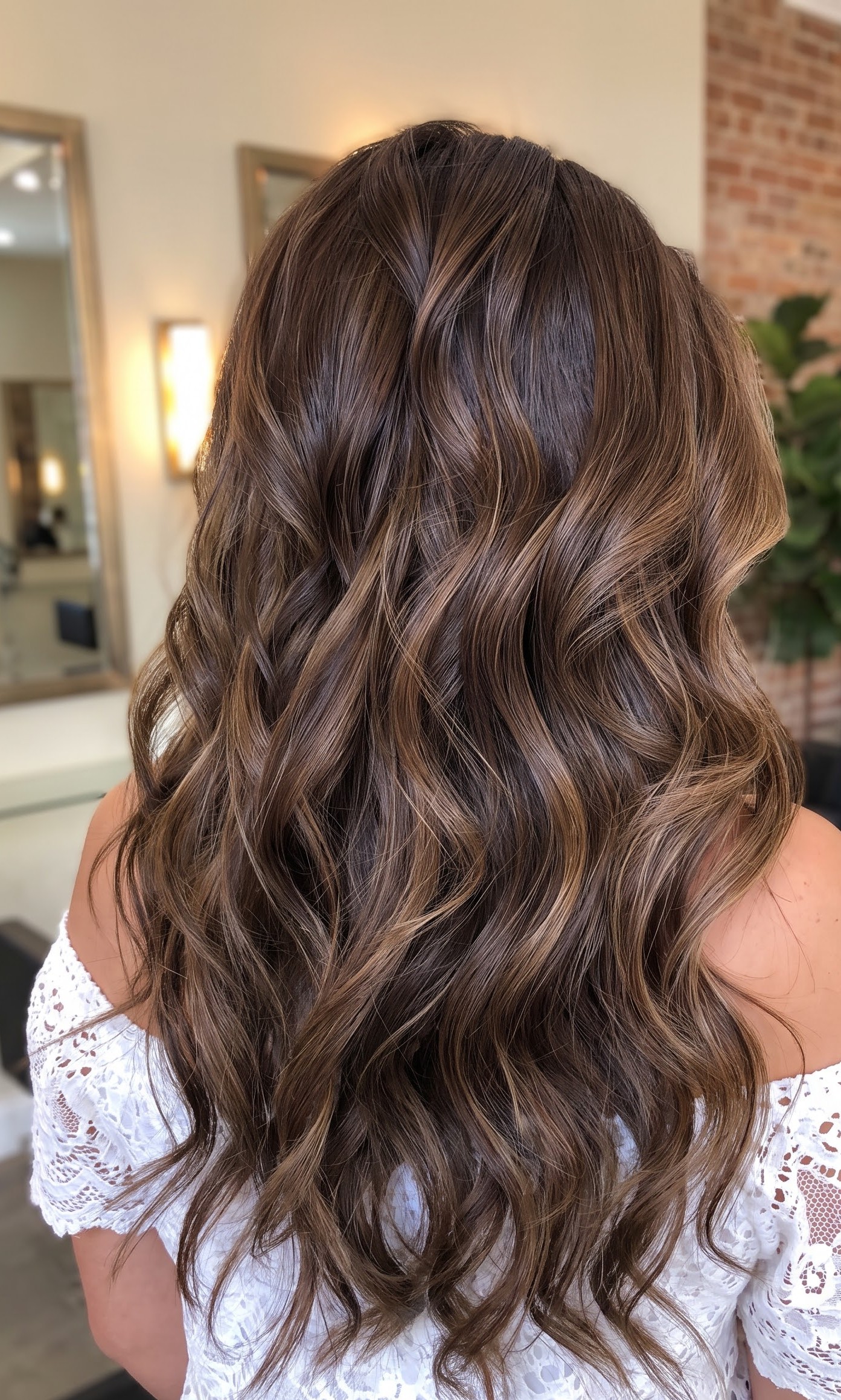 Brunette hair with caramel balayage highlights styled in loose curls, worn with a white lace top