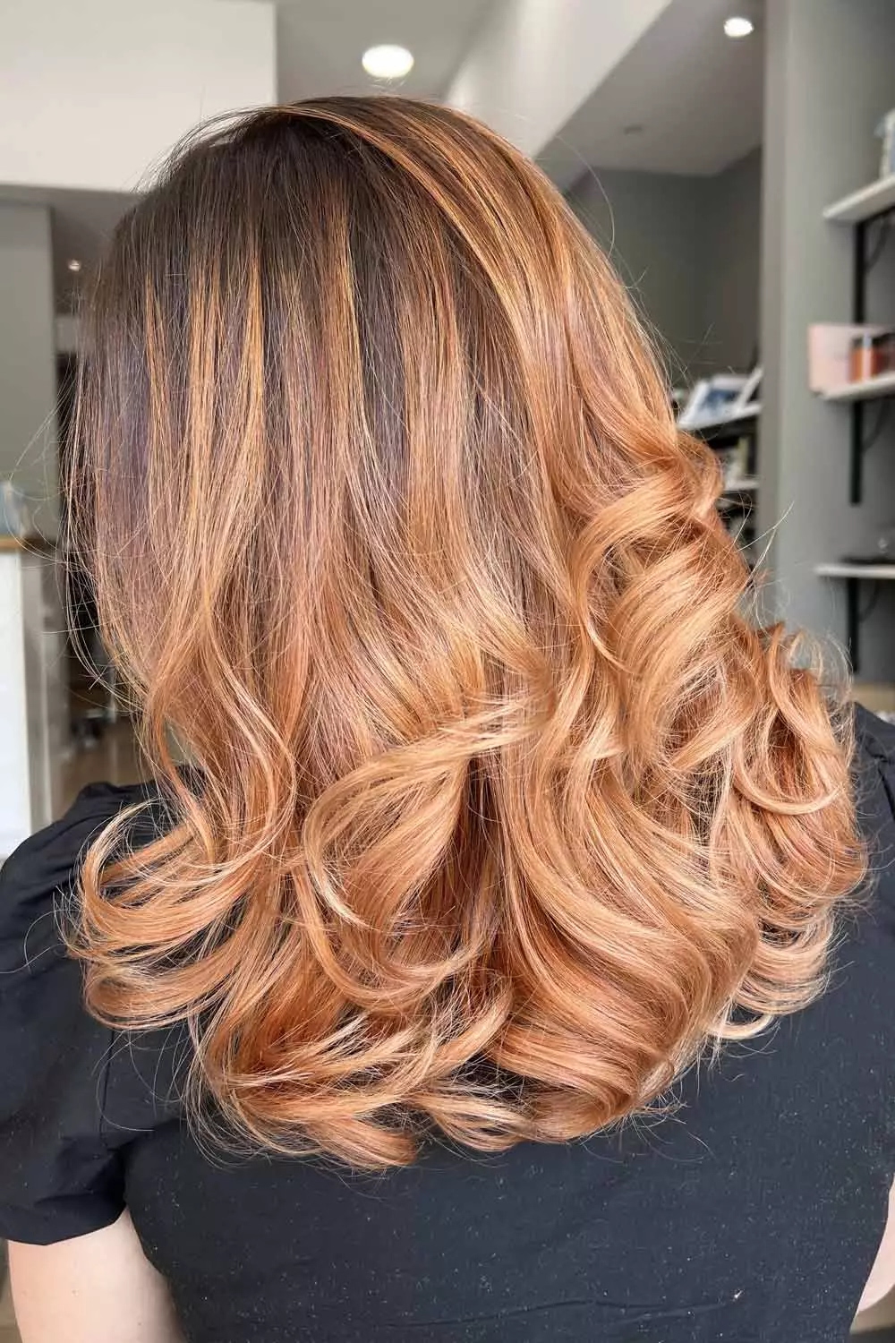 Copper balayage hair styled in soft curls in a bright, naturally lit salon studio