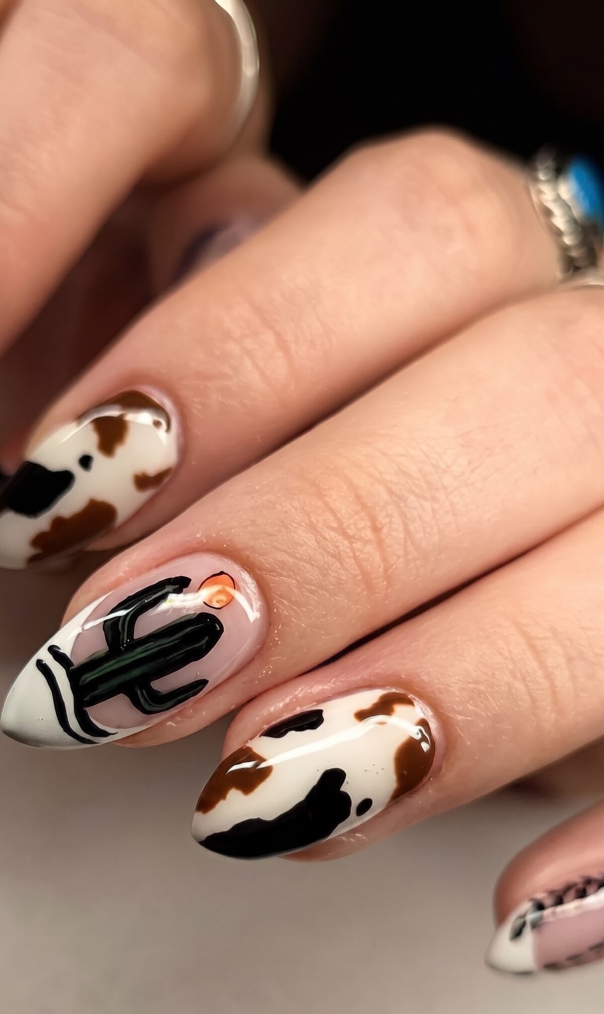 Cow print nails with a hand painted cactus and desert sun accent nail