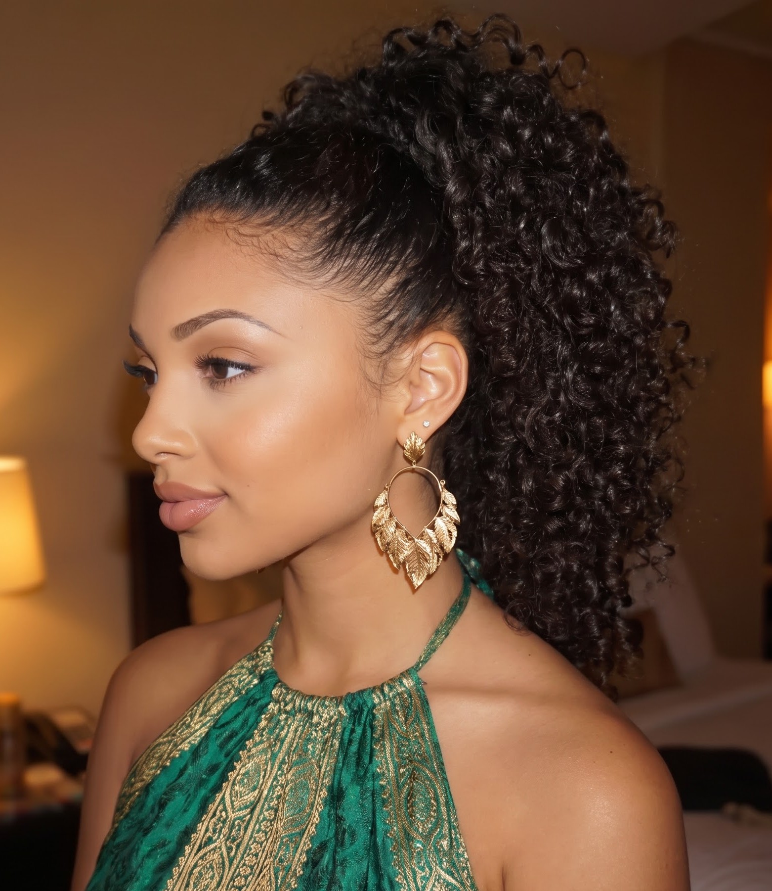 Dark curly hair styled in a sleek high ponytail with gold statement earrings and a green dress