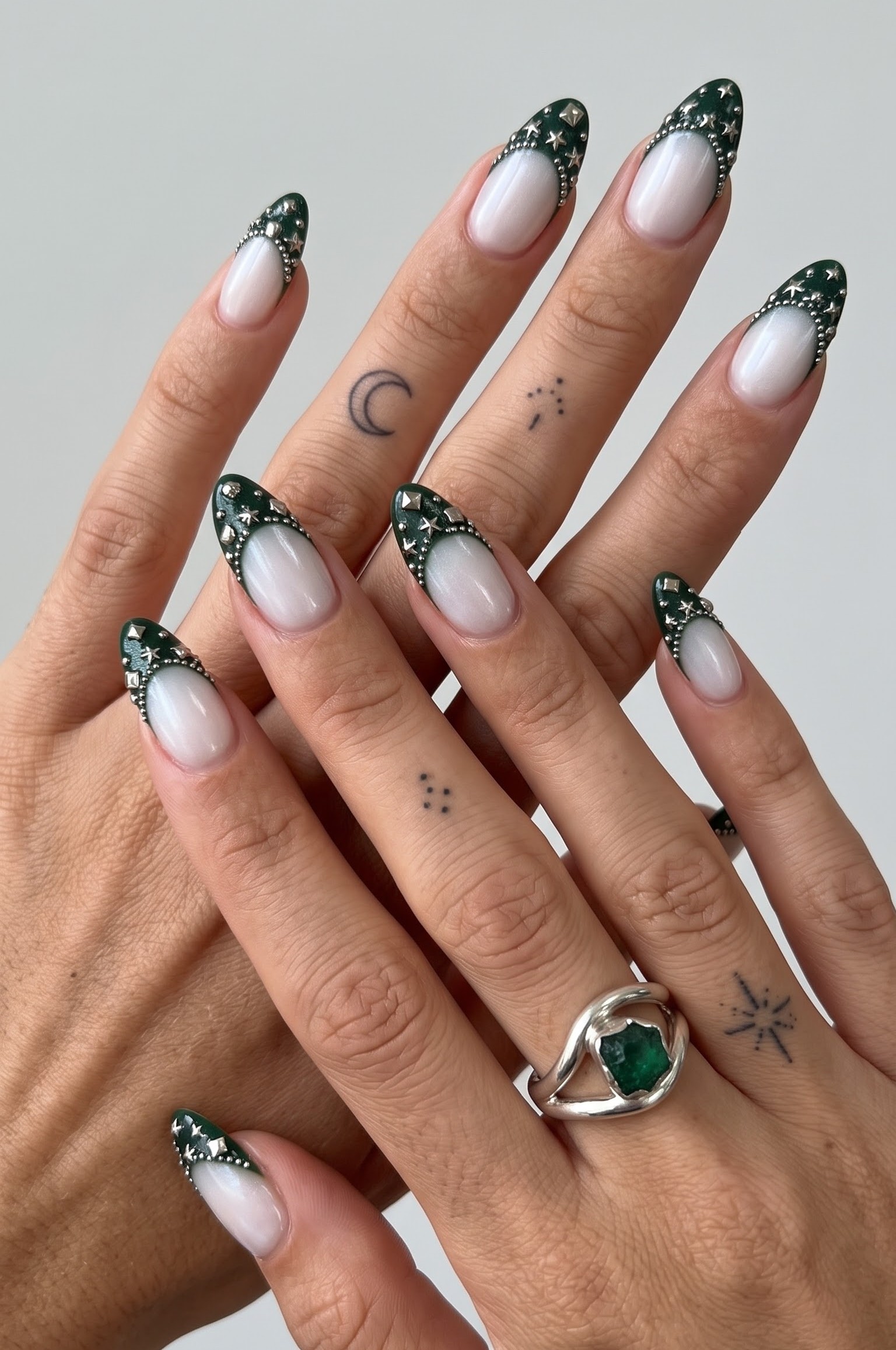 Pearlescent white nails with dark emerald french tips and silver star studs