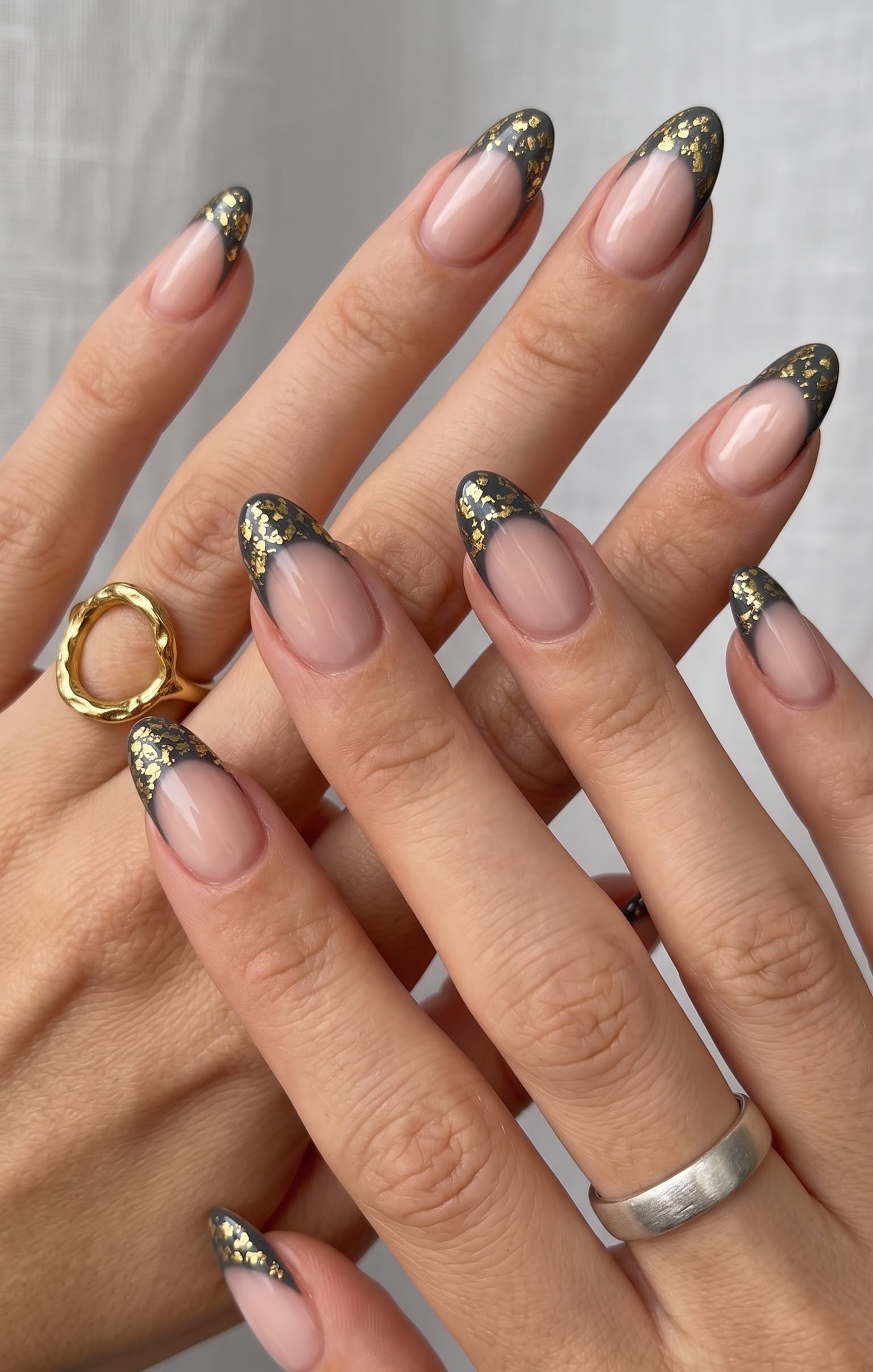 Nude almond nails with charcoal grey french tips and gold foil flakes