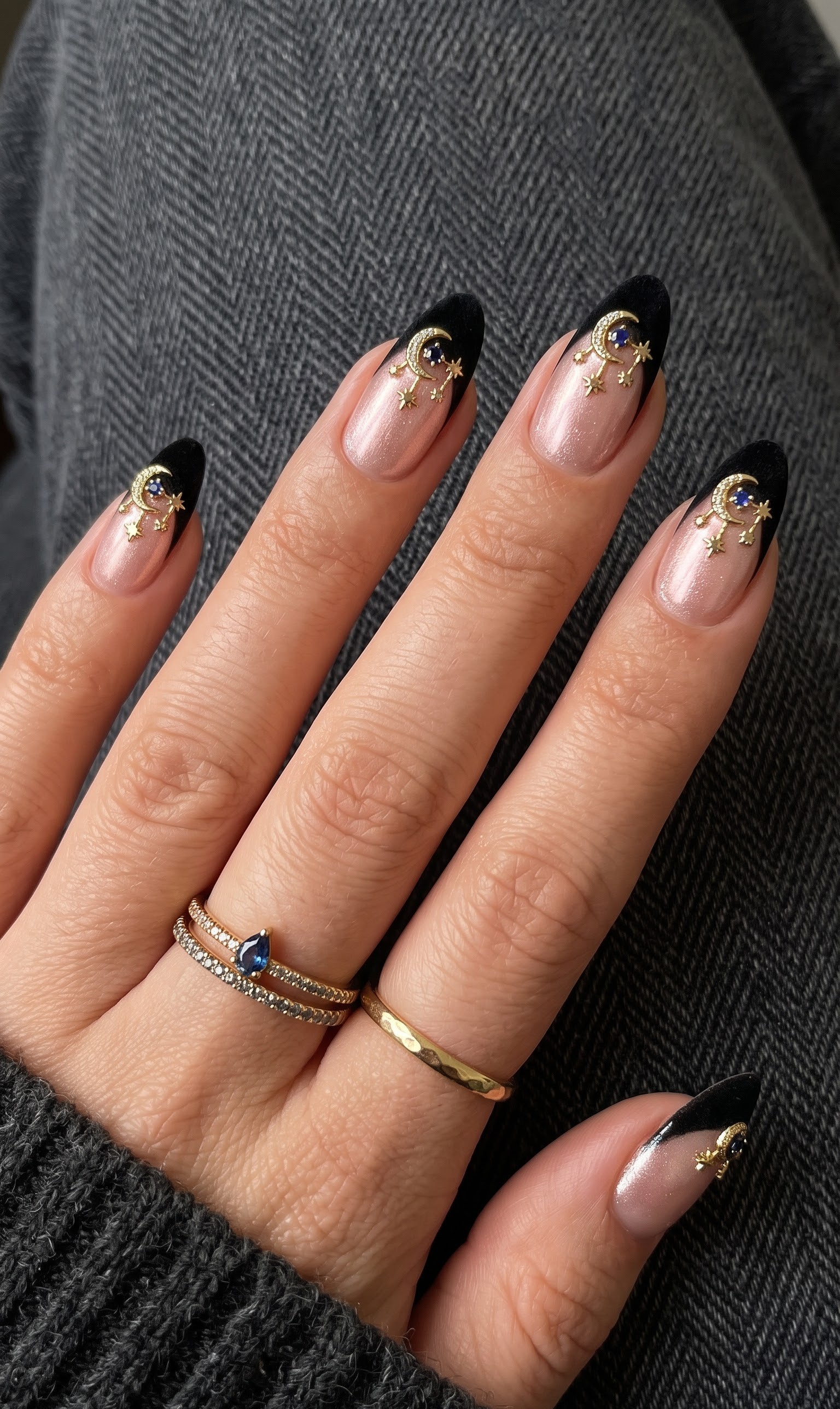 Shimmering pink almond nails with matte black french tips and gold crescent moon star charms