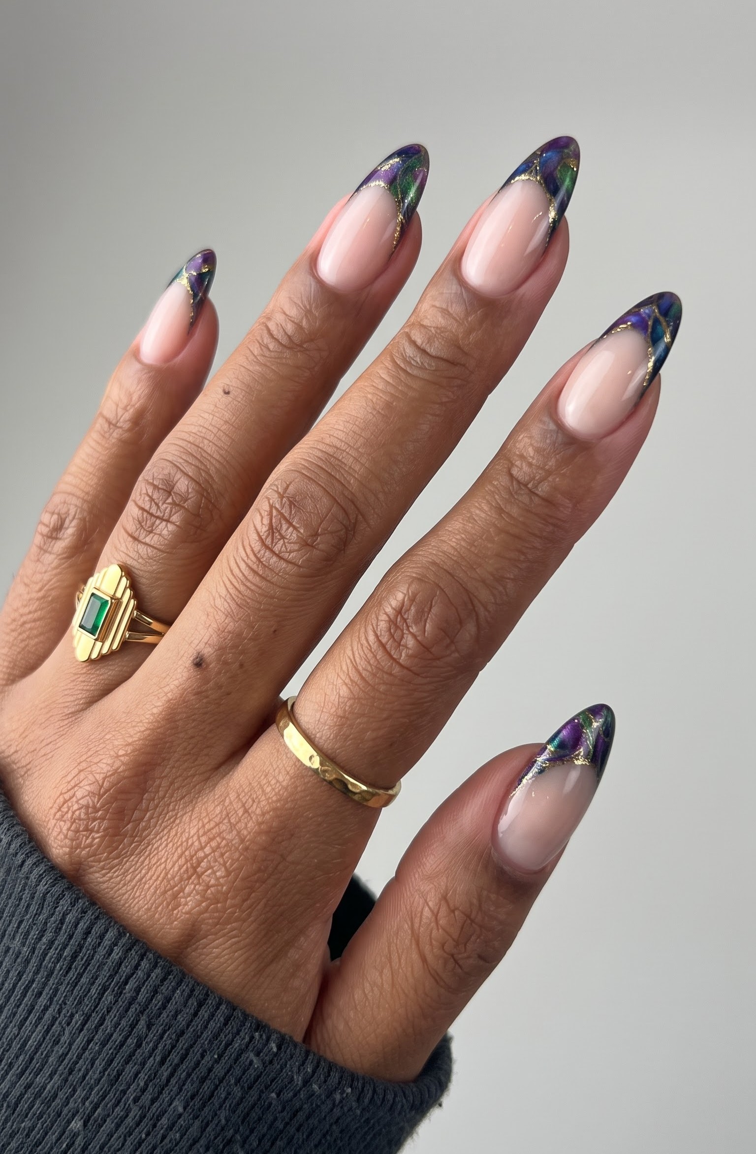 Nude almond nails with purple, green and blue stained glass style french tips outlined in gold