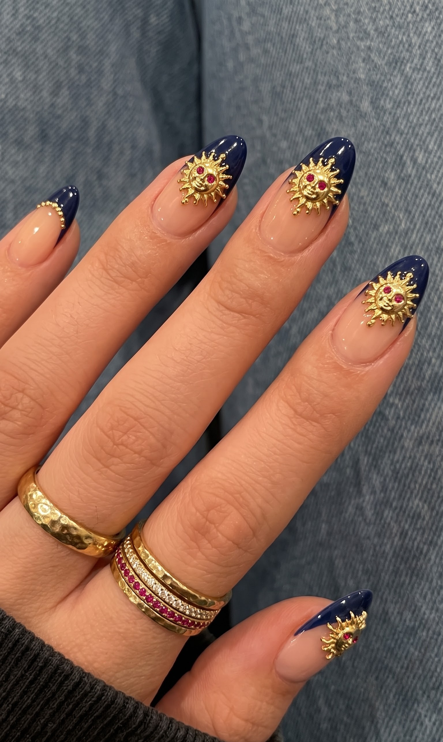 Nude almond nails with navy blue french tips and 3D gold sun face charms
