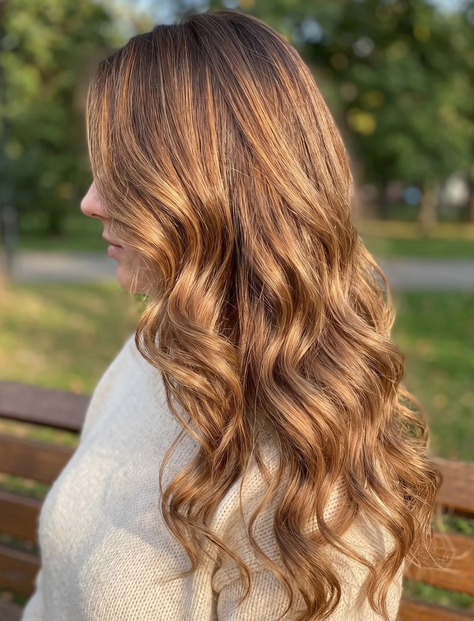 Golden copper balayage hair styled in loose waves, glowing in outdoor sunlight
