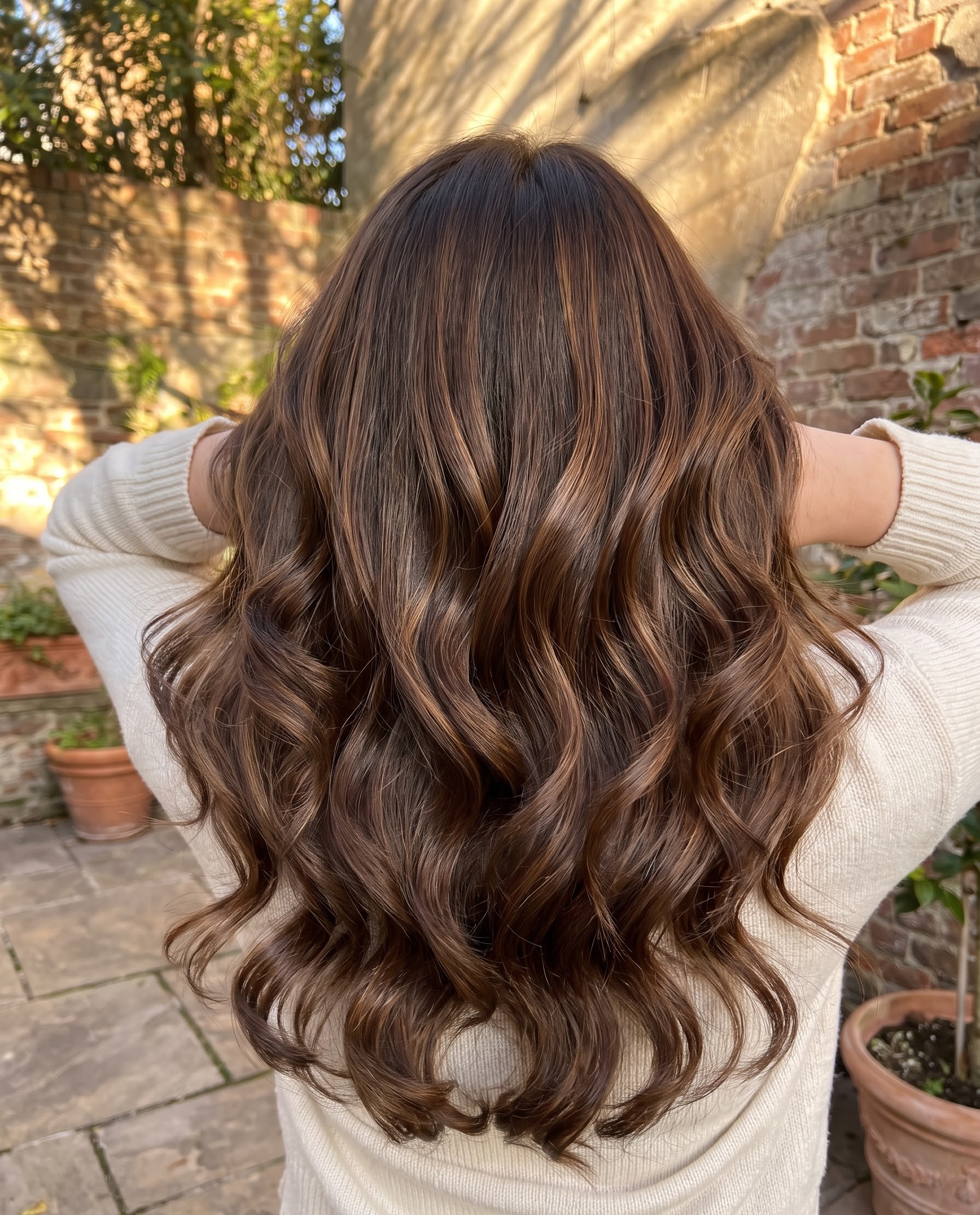 Brunette hair with caramel balayage highlights styled in curls, photographed outdoors in golden hour light