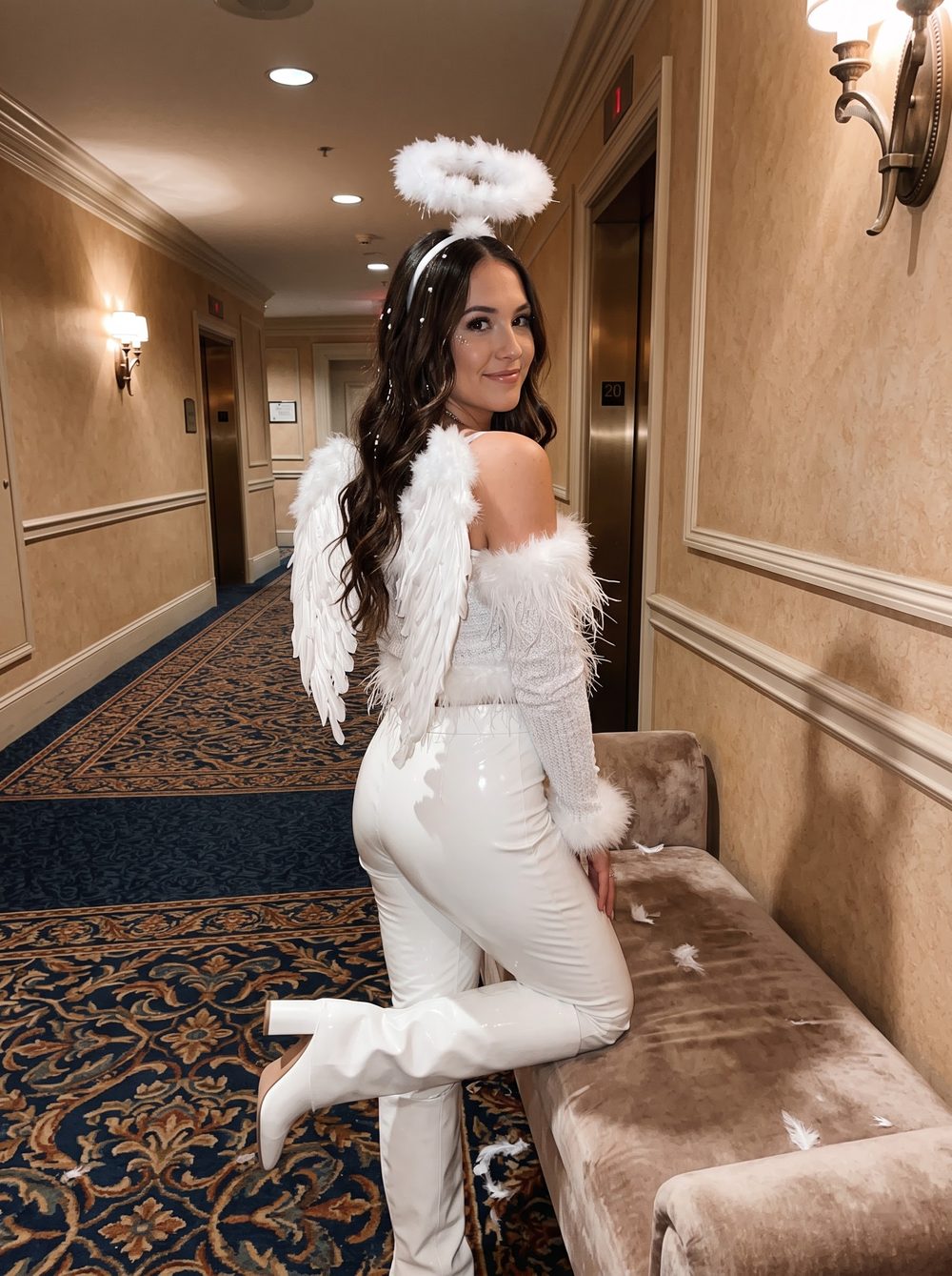 Woman in a white angel costume with feather wings, a fluffy halo headband, feather-trim top and white patent pants in a hotel hallway