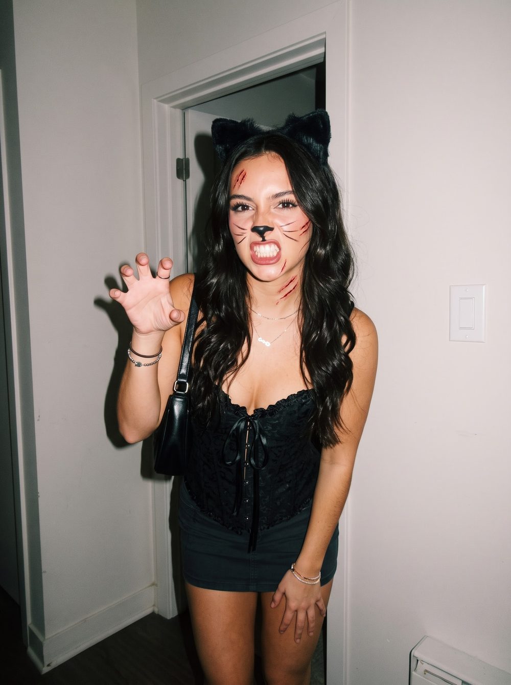 Woman in a black cat costume with fluffy ears, painted whiskers and nose, claw scratches and a black lace corset top