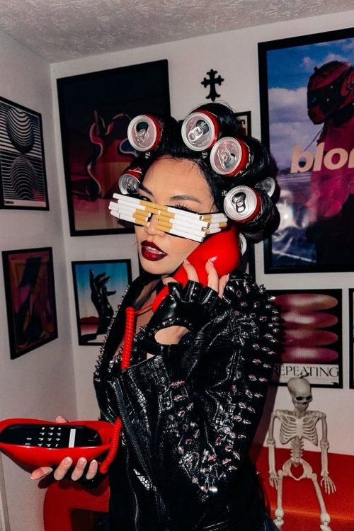Woman in a Lady Gaga Telephone inspired costume with soda can hair curlers, cigarette glasses, a red telephone and a black spiked leather jacket