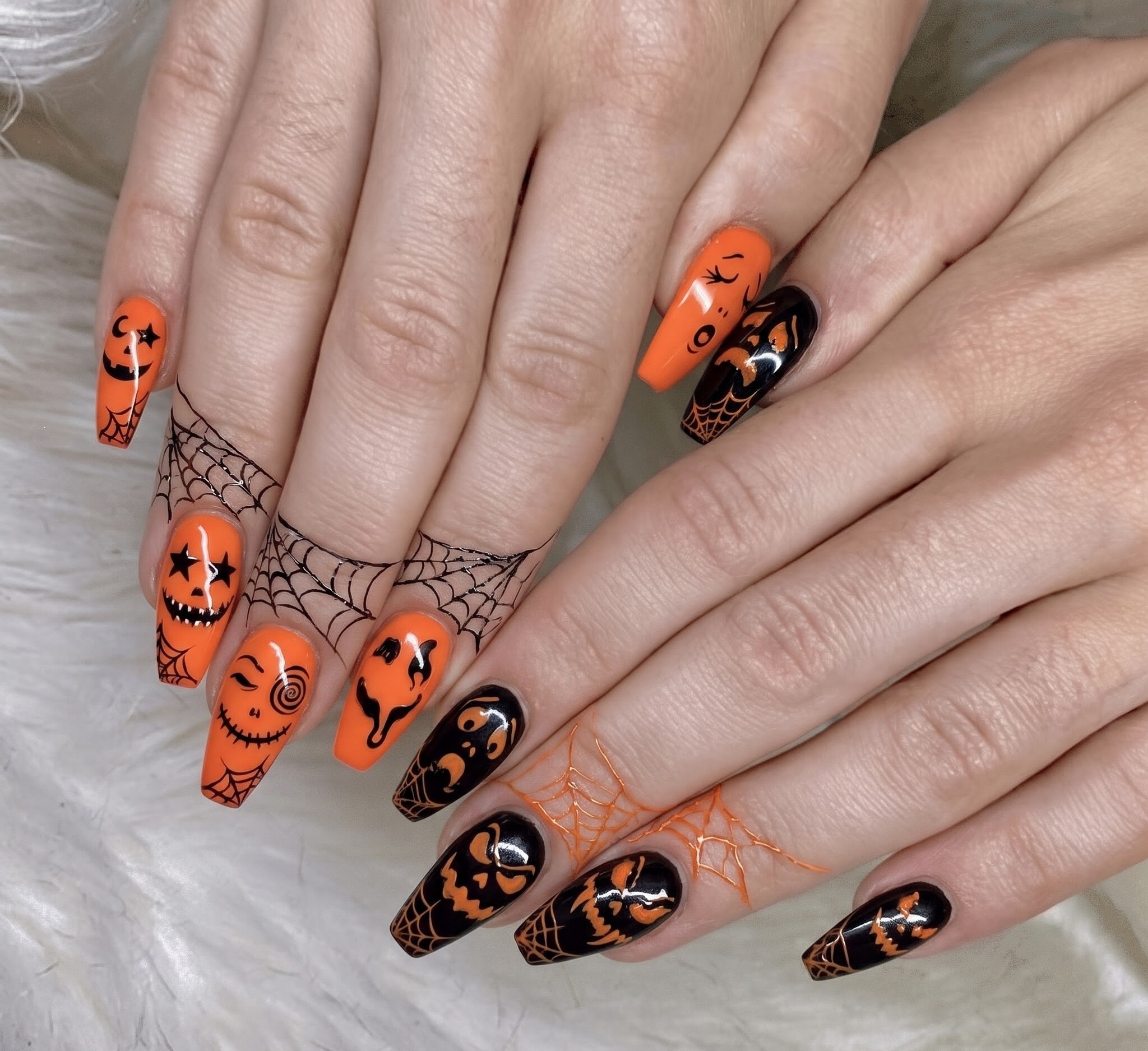 Orange and black Halloween nails with jack o lantern faces and spiderwebs