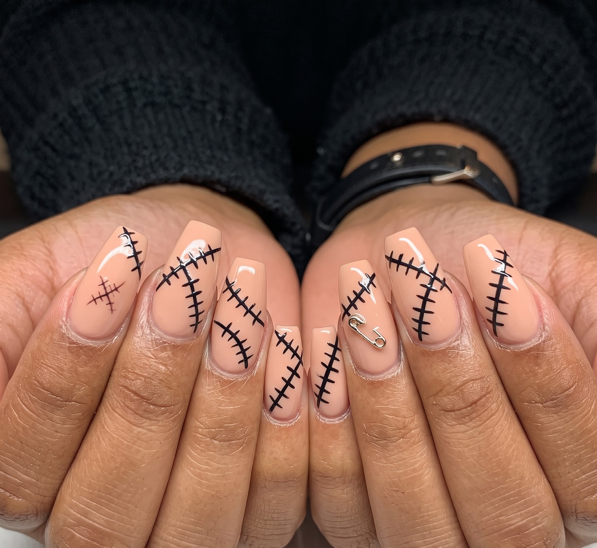 Nude Halloween nails with hand painted black stitch outlines and a safety pin charm