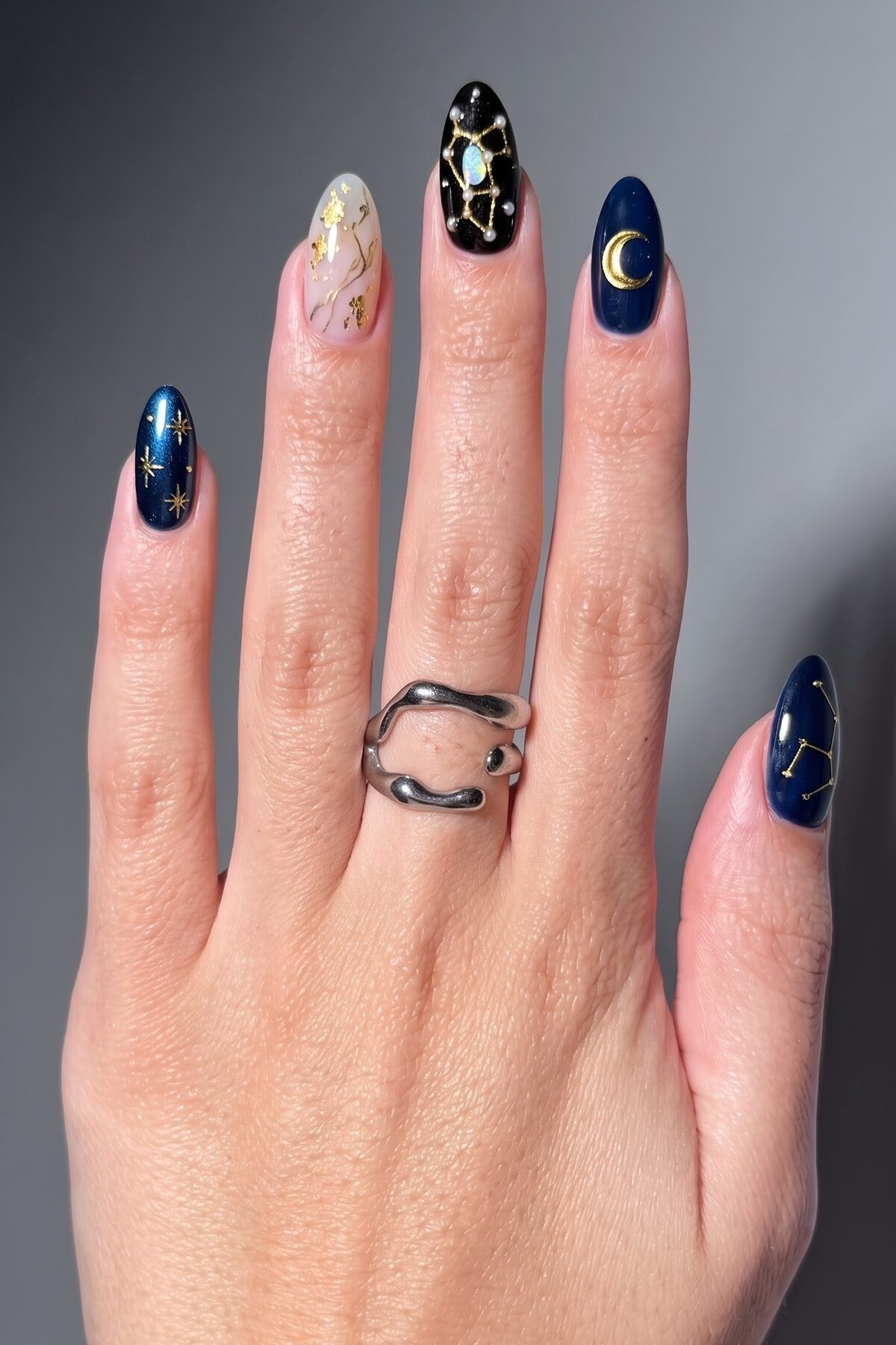 Navy blue nails with gold stars, a crescent moon, constellation art and a black opal accent nail