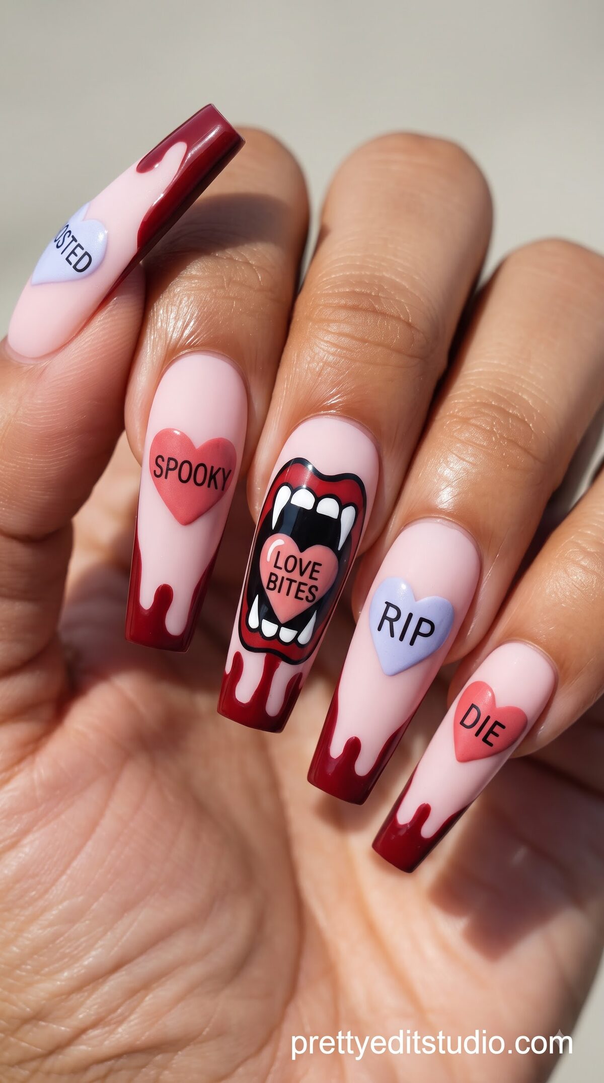 Pink nails with dripping red tips, conversation heart candies reading SPOOKY, RIP, and a vampire mouth design